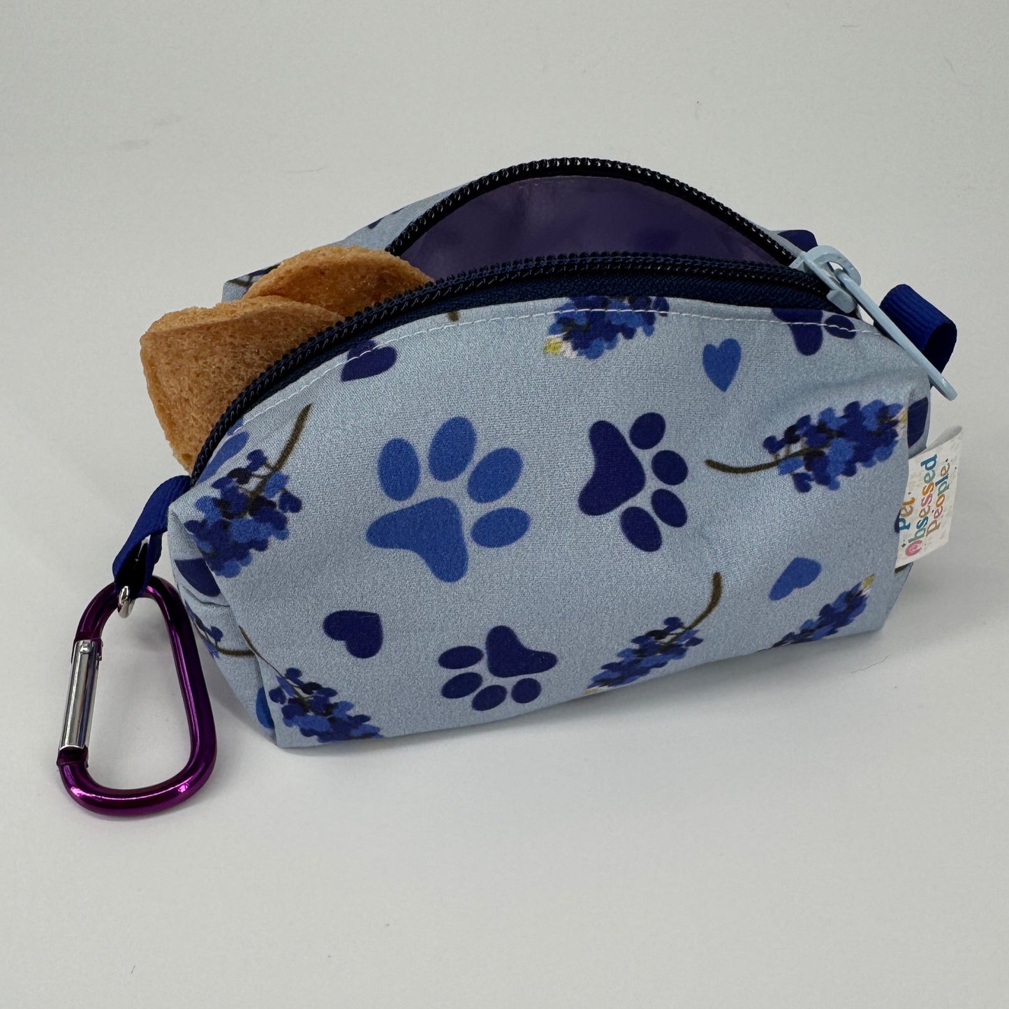 Small treat pouch with blue paw prints and floral patterns on a light gray background